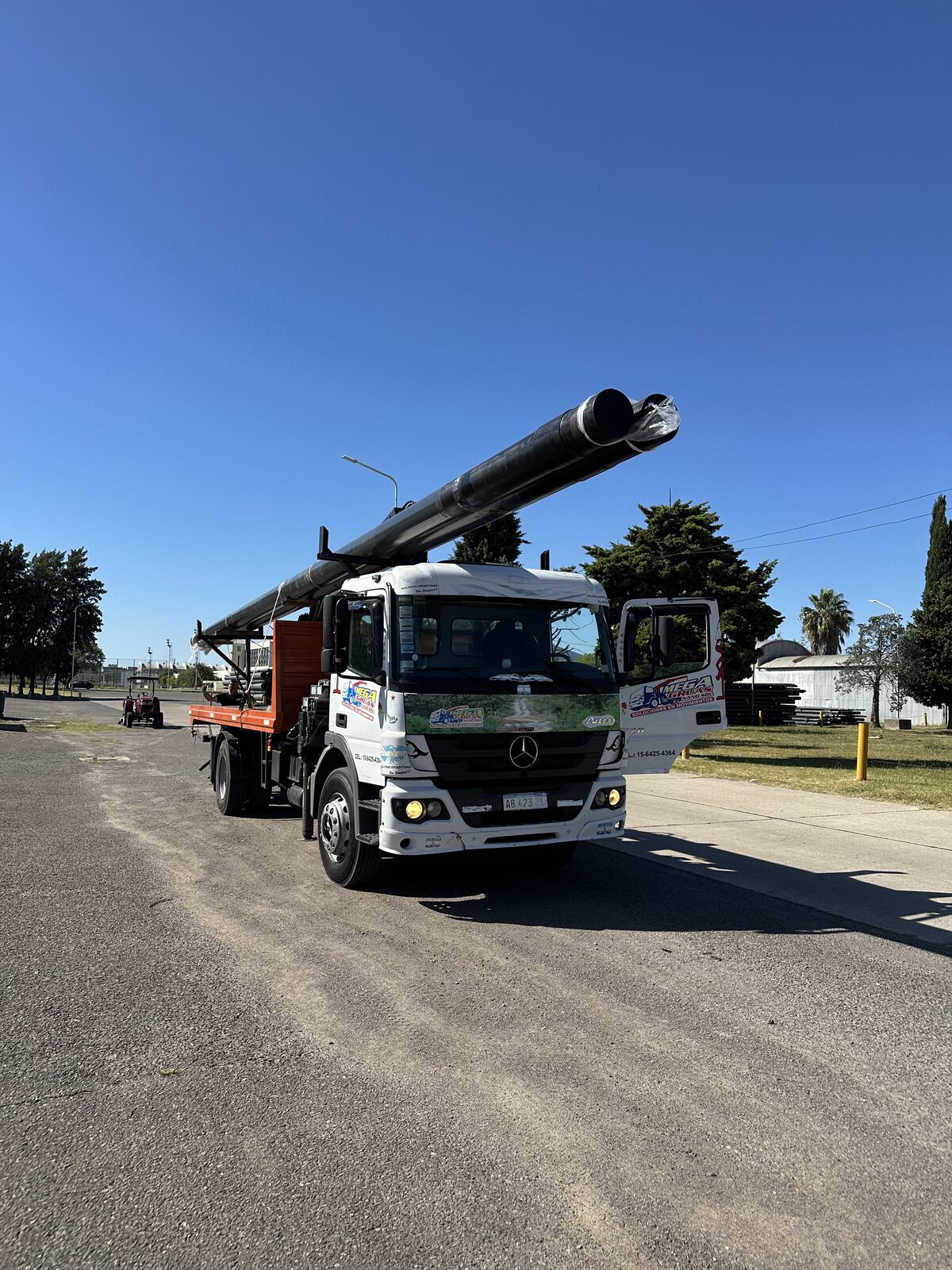 Mercedes-Benz Atego blanco transportando caños metálicos largos